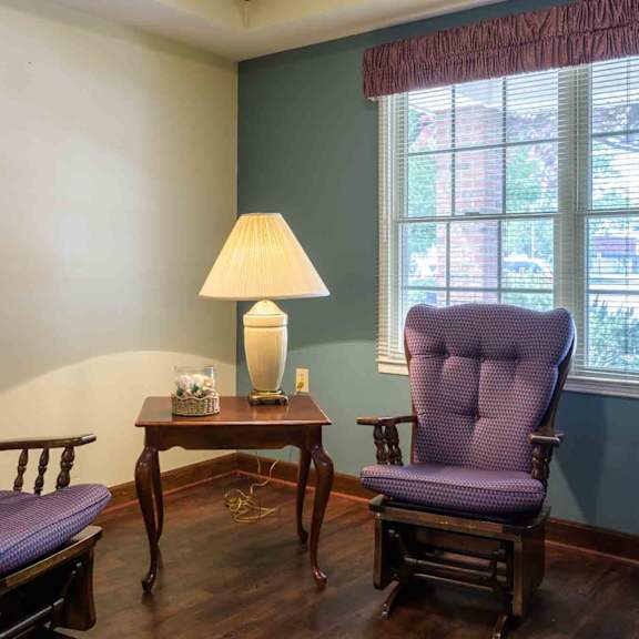 two purple chairs sit in front of a table with a lamp on it.