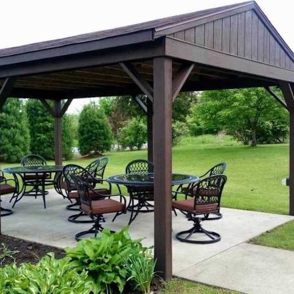 a wooden pavilion with a table and chairs set up outside.