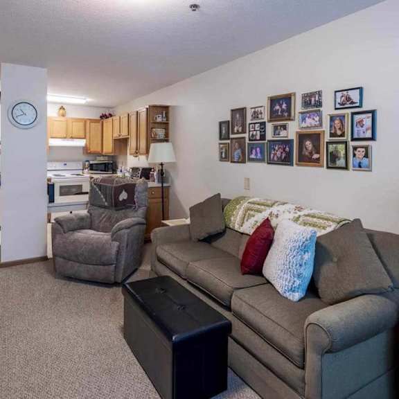 a living room with a grey couch, a black coffee table, and a white clock on a pillar.
