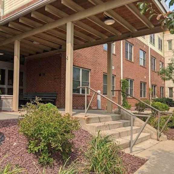 a building with a red brick facade and a wooden pergola over a set of stairs.