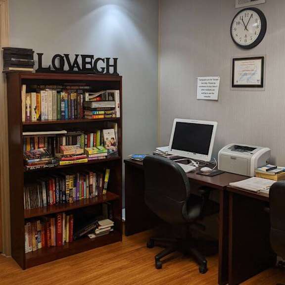 a room with a bookshelf, a desk with a computer, and a clock on the wall.