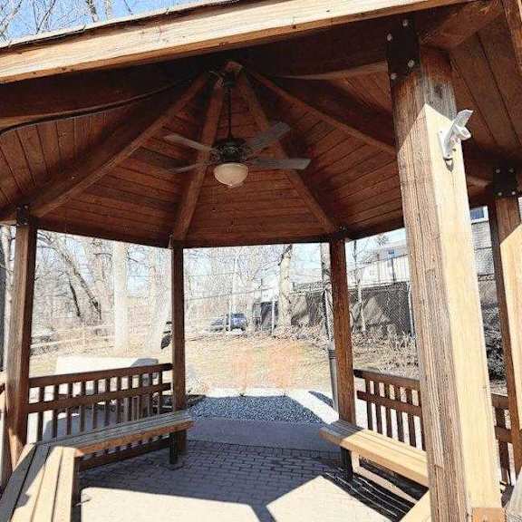 a wooden gazebo with a ceiling fan is surrounded by benches.