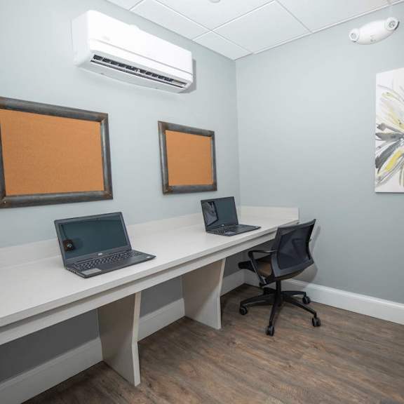 a room with a white desk, two laptops, and two empty picture frames.