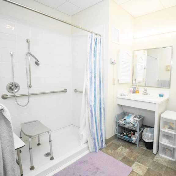 a bathroom with a white toilet, a white sink, a purple rug, and a shower with a blue and white striped shower curtain.