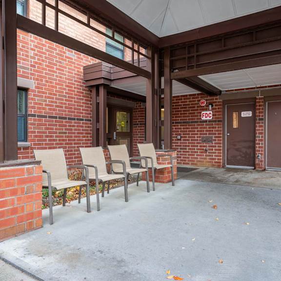 a covered walkway with chairs and a brick wall.