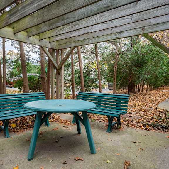 a green bench and table are set up under a wooden canopy in a park.