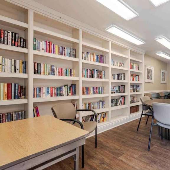 a room with a long bookshelf filled with books and a table with chairs in front of it.