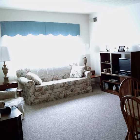 a living room with a sofa, a chair, a table, a lamp, a television, and a bookshelf.