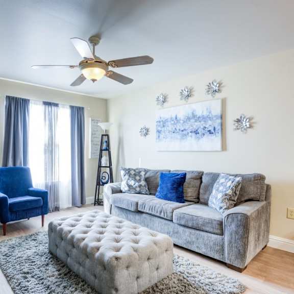 a living room with a grey couch, blue chair, and a ceiling fan.