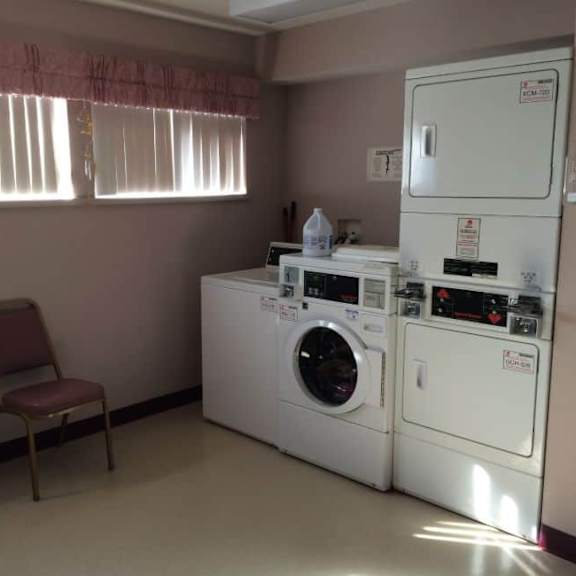 a laundry room with a washer and dryer, a chair, and a window with blinds.
