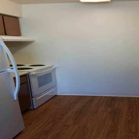 a kitchen with a white fridge, stove and oven, and a wooden floor.