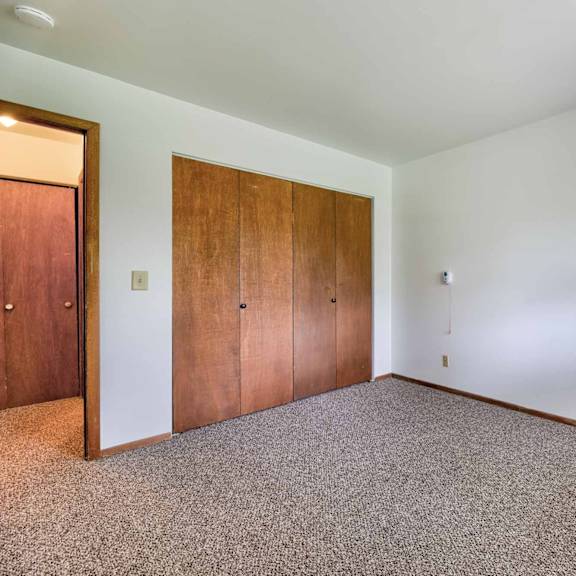 a room with a window, carpeted floor, and two wooden doors.