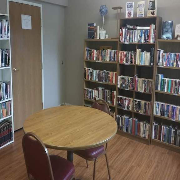 a room with a table, chairs and bookshelves filled with books.