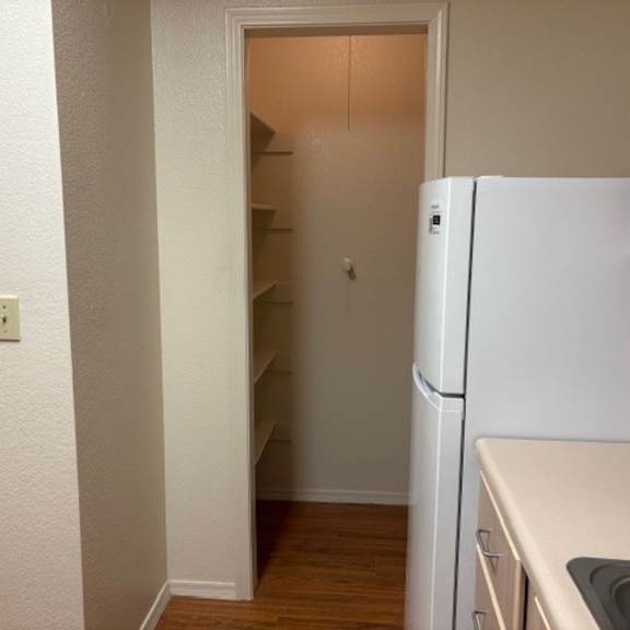 a white refrigerator in a kitchen with wooden floors and white walls.