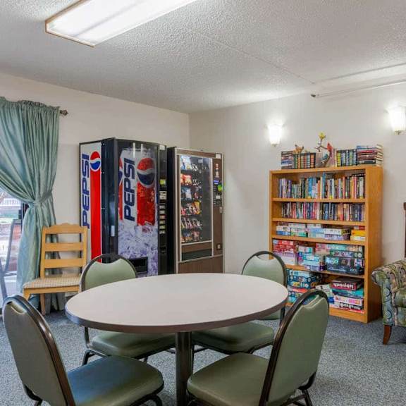 a room with a round table, chairs, a bookcase, and a pepsi fridge.