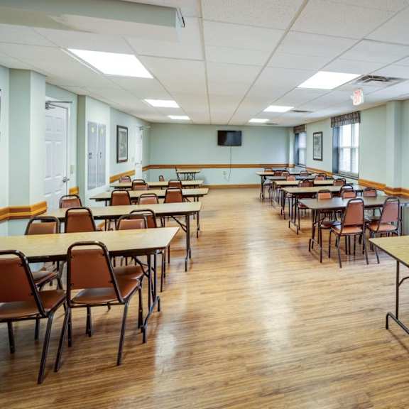 a room with tables and chairs and a tv on the wall.