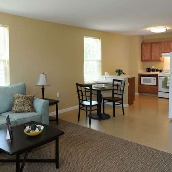 a living room with a grey couch, a black coffee table, and a dining area in the background.