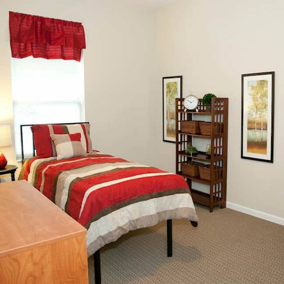 a bedroom with a bed, desk, chair, and two pictures on the wall.