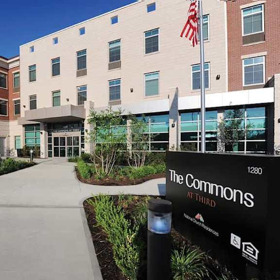 the commons at third is a modern building with a flag flying in front.