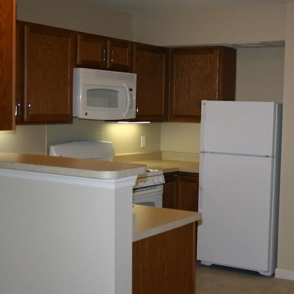 a white refrigerator stands in a kitchen with wooden cabinets and a white microwave above the stove.