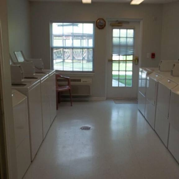 a laundromat with washers and dryers is empty except for one washer and dryer in the back.