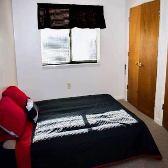 a bedroom with a bed, a window with blinds, and a red chair.