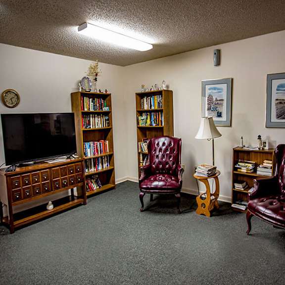 a living room with a television, two chairs, a bookshelf, and a clock.