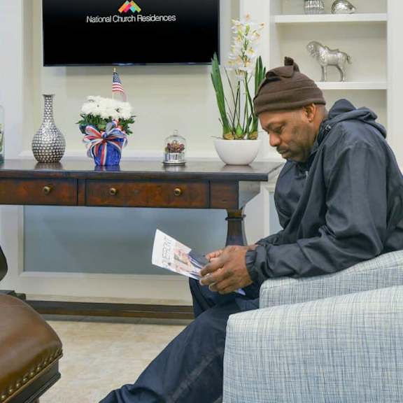 a man in a black hoodie is sitting on a blue chair and reading a paper.