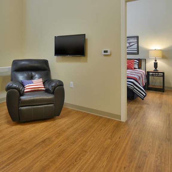 a black leather chair with an american flag pillow sits in a room with wood floors and a flat screen tv mounted on the wall.