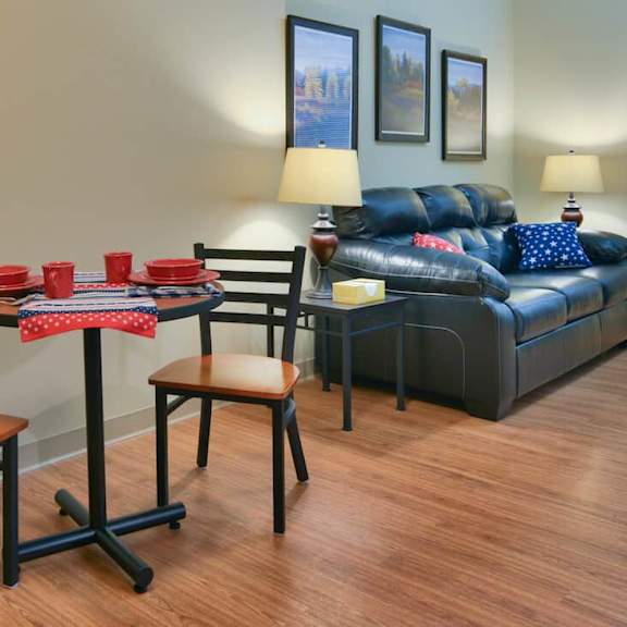 a living room with a black couch, a small table with a red cloth, and two chairs.