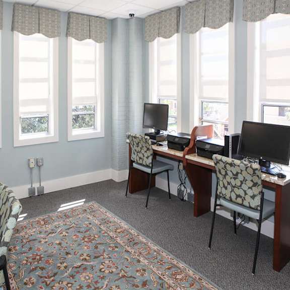 a room with a desk and chairs with a window in the background.
