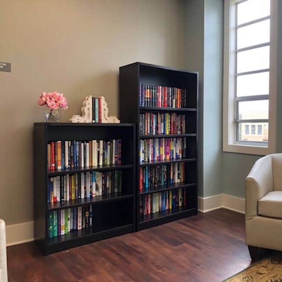 a living room with a bookshelf, a chair, and a vase of flowers.