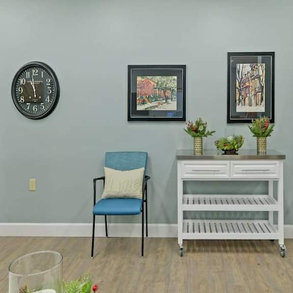 a chair with a blue cushion is placed in front of a wall clock and two framed pictures.