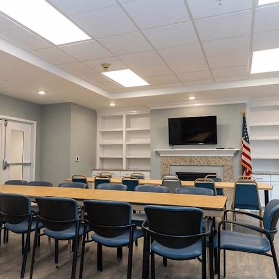 a conference room with a long table, chairs, and a television mounted above a fireplace with an american flag.