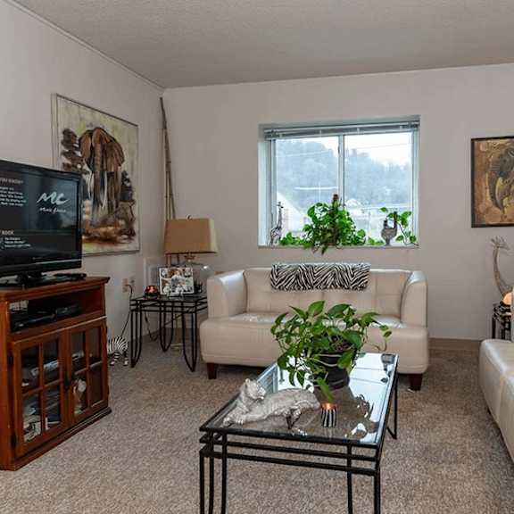 a living room with a white couch, a glass coffee table, and a television.