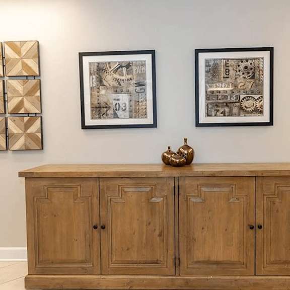 a wooden cabinet with a decorative item on top and two framed pictures on the wall.