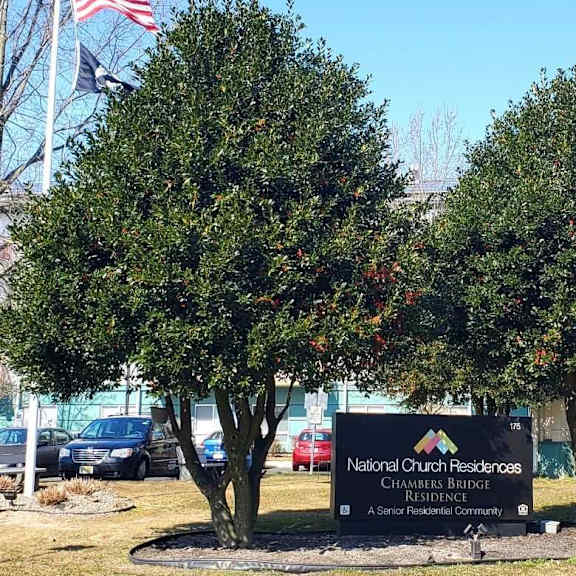a sign for national church residences chambers bridge is in front of some trees.