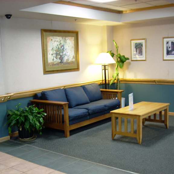 a blue couch sits in a waiting room with a wooden coffee table and a lamp.