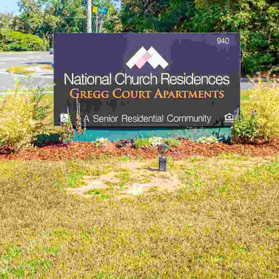 a sign for national church residences gregg court apartments is in front of a grassy area.