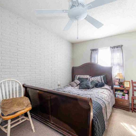 a bedroom with a bed, chair, and a ceiling fan.