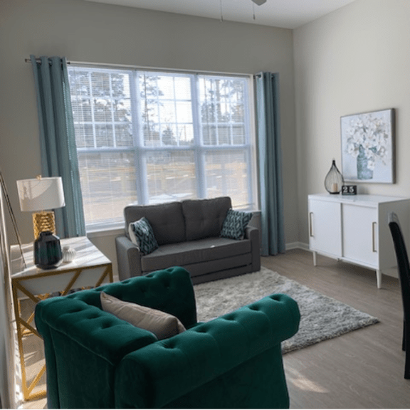 a living room with a grey couch, a green armchair, a white side table, and a black chair.