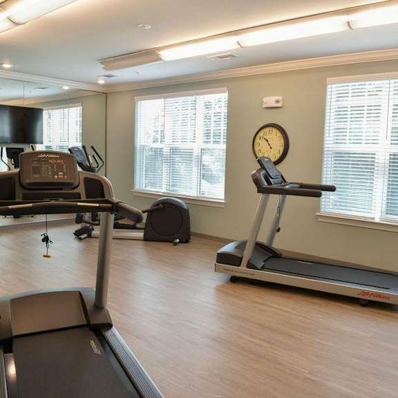 a treadmill and a stationary bike are in a well-lit room with a clock on the wall.