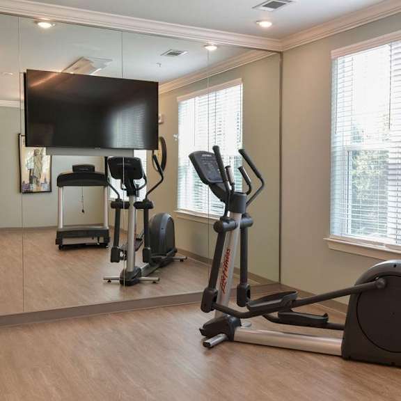 a home gym with a treadmill, elliptical trainer and a television.