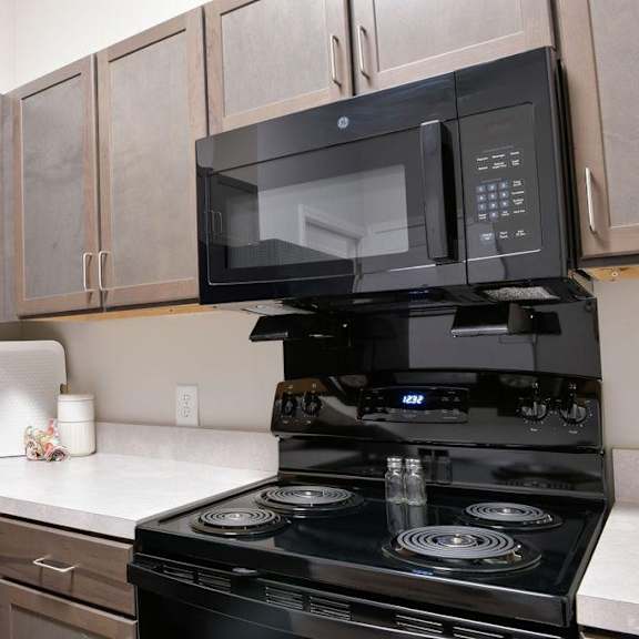 a black microwave oven is mounted above a black stove in a kitchen.