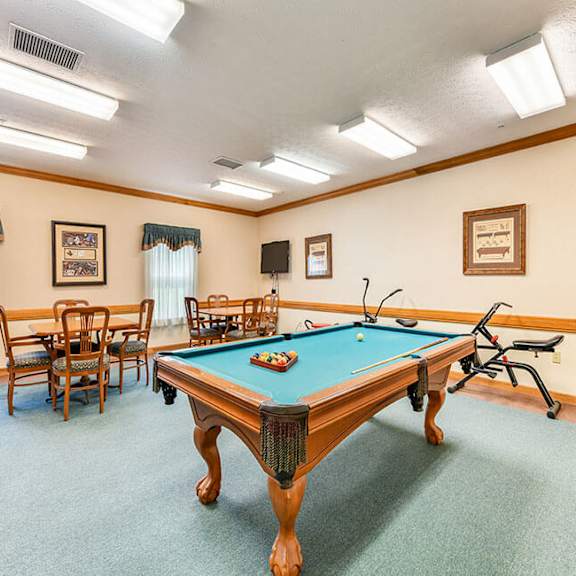 a pool table is in the middle of a room with chairs and pictures on the wall.