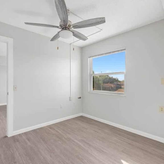 a room with a ceiling fan and a window showing a view of trees.