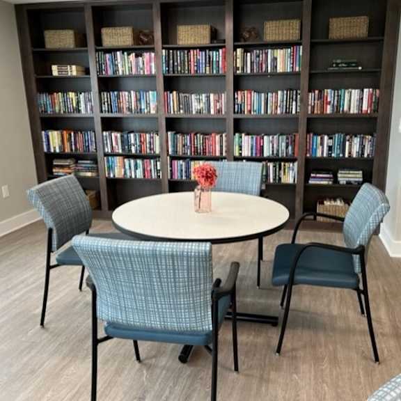a room with a round table and chairs in front of a bookshelf.