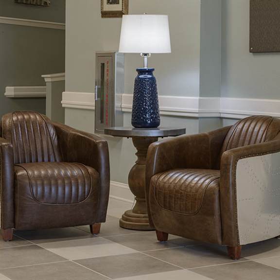 two brown leather chairs are placed in front of a table with a blue lamp on it.