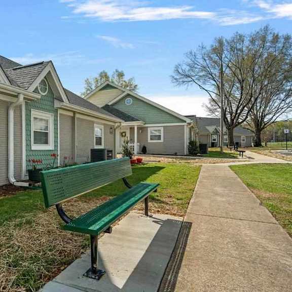 a green bench sits in front of a building with a row of houses behind it.