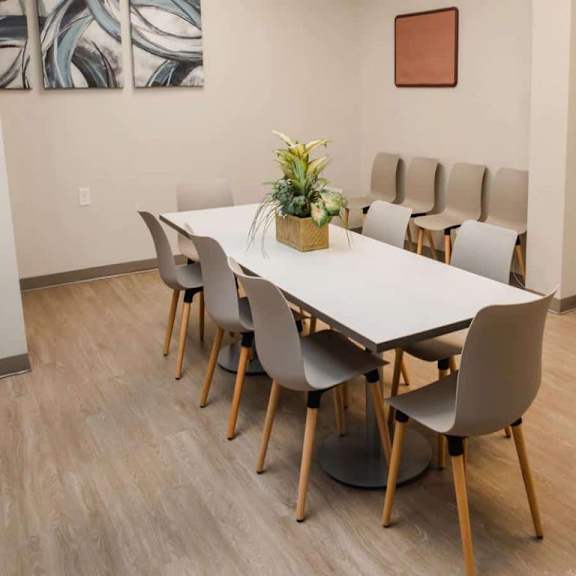 a white table surrounded by grey chairs with a plant on top.